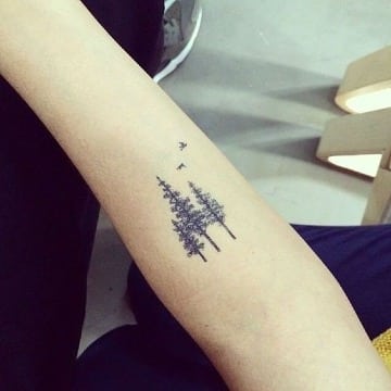 pequeños tatuajes de pinos en el antebrazo