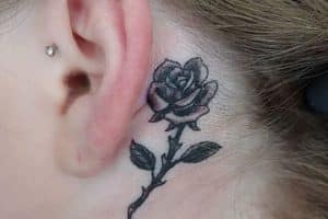 tatuaje rosa detras de la oreja con tallo y espinas